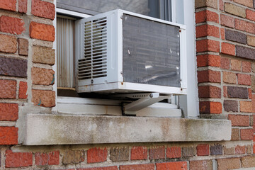 exterior view of air conditioning window unit extruding from the window sill of a red brick building with a portable safety ledge support installed under it