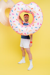 Full length of positive sportsman holding swim rings on yellow background.