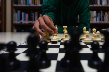 hand moving a chess piece (a pawn), playing on a library