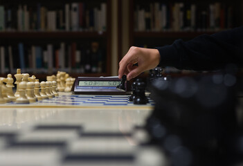 hand moving a chess piece (a pawn), playing on a library