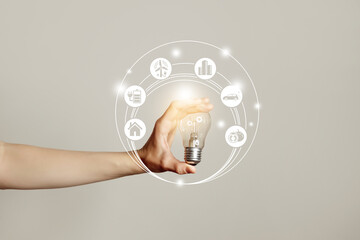 Woman`s hand holding glowing light bulb with energy resources icons. Ecological friendly and sustainable environment concept..Electricity and energy saving, energy sources.