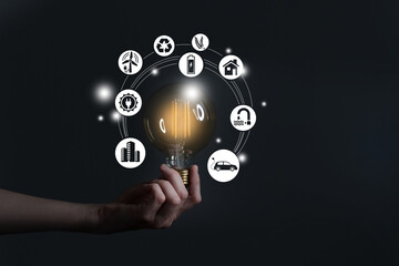 Woman`s hand holding glowing light bulb with energy resources icons. Ecological friendly and sustainable environment concept..Electricity and energy saving, energy sources.