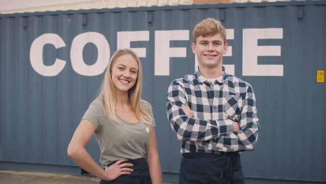 Smiling male and female interns at freight haulage business standing outdoors in front of shipping container labelled coffee - shot in slow motion