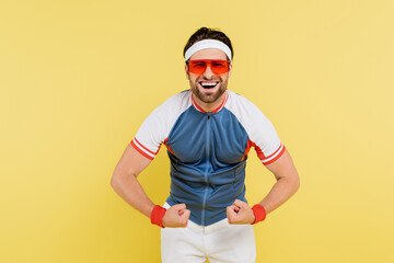 Cheerful sportsman showing muscles isolated on yellow.