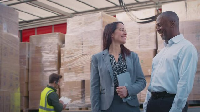 Smiling male and female managers standing next to truck being loaded at distribution warehouse holding digital tablet looking into camera -shot in slow motion