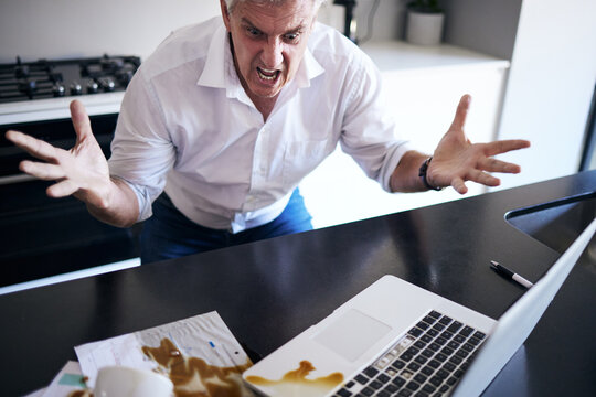 What The Heck Just Happened. Shot Of A Mature Man Feeling Angry After Spilling Coffee On His Paperwork And Laptop In The Kitchen At Home.