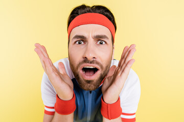 Portrait of shocked sportsman looking at camera isolated on yellow.