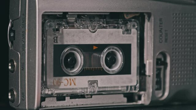 Audio Cassette in the Tape Recorder Playing and Rotates. Close-up. Vintage transparent tape with a blank label spinning in the audio player. Call recording on portable handheld retro microcassette.