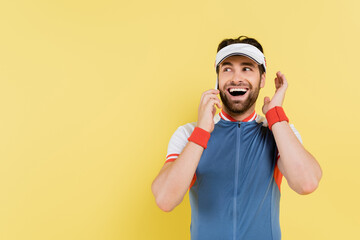 Cheerful sportsman talking on smartphone isolated on yellow.