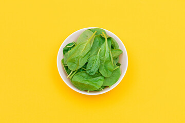 Fresh Baby Spinach Leaves in White Bowl on Yellow Background - Top View. Vegan and Vegetarian Culture. Raw Food, Green Leaves. Healthy Diet