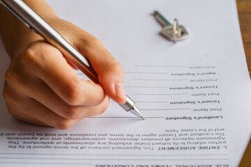 Naklejka premium Lease agreement document concept. Landlord is signing the lease document paper with pen and key, Rental agreement form, signing hand, agreement.