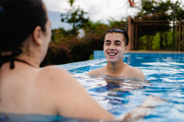 latin teenager laughing in an infinity pool with his mother