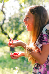 Defocus beautiful smiling teenage girl in dress smiling against green summer background. Abstract summer background. Teen girl holding raspberries fruit. Close-up portrait. Out of focus