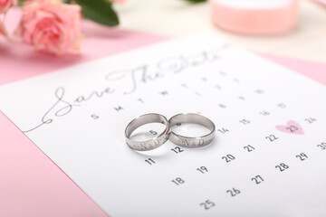 Wedding rings with engraved initials and calendar on table, closeup