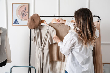 Young woman near rack with stylish clothes in studio