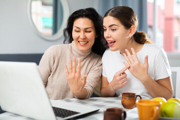 Two adult female friends positively communicate via internet using laptop at home