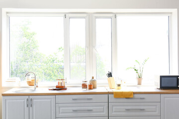 Counter with microwave oven, sink, products and utensils in interior of modern kitchen with window