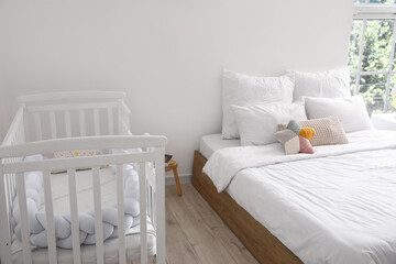 Big bed and comfortable baby crib in interior of cozy room