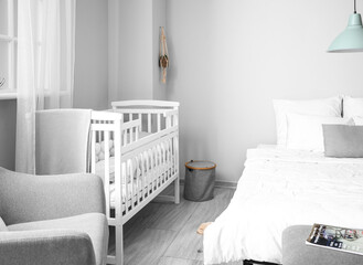 Modern interior of cozy room with big bed and comfortable baby crib