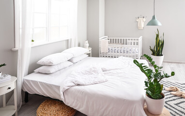 Modern interior of cozy room with big bed and comfortable baby crib