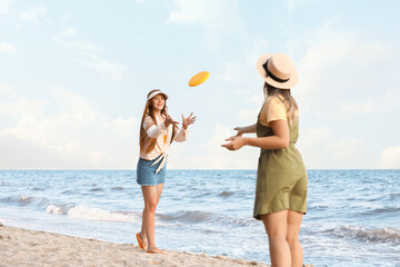 Happy young women playing frisbee on sea beach