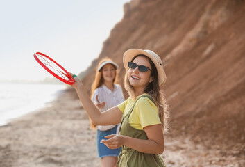 Happy young woman with friend playing frisbee on sea beach