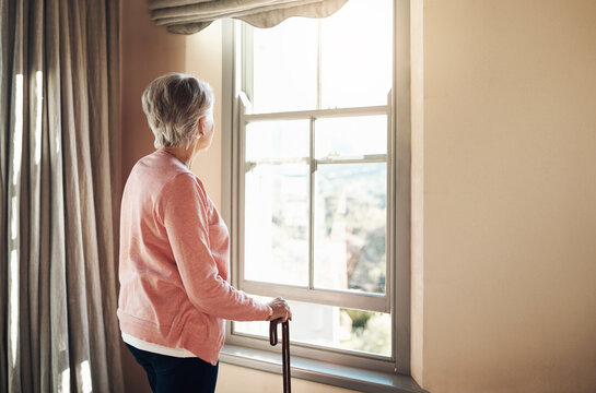 When did the days become so grey. Shot of a senior woman with a cane looking thoughtfully out of a window at home.