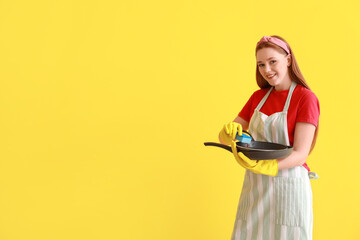 Young woman with sponge and dirty frying pan on color background