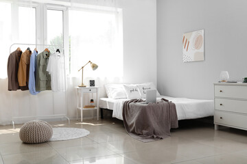 Rack with stylish clothes in interior of light bedroom