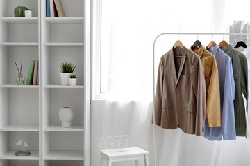 Rack with stylish clothes and shelving unit near light curtains