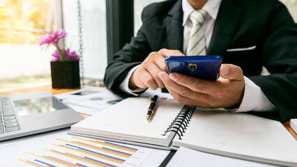 Businessman hand holding a smartphone, working on project statistics on devices. Presentation with graphs and an entrepreneur's accountant laptop analyzes financial data. show changes in the market