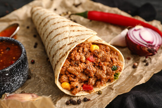 Parchment with tasty burrito, sauce and spices on table, closeup