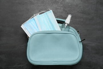 Female bag with medical masks and bottle of antiseptic on dark background
