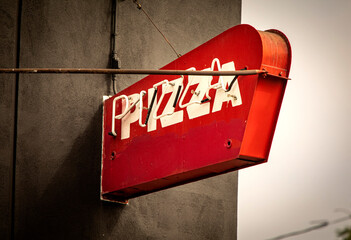 Neon red sign with white letters on a black wall stating pizza