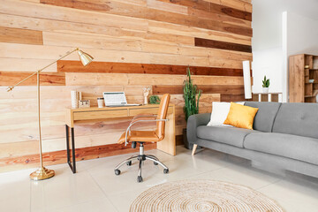 Interior of stylish room with modern workplace, sofa and wooden wall