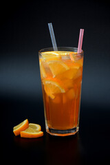 A tall glass of fresh orange juice with ice and citrus pieces on a black background.