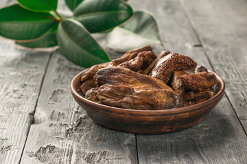 A bowl with dried bananas on a background of green leaves on a wooden table.