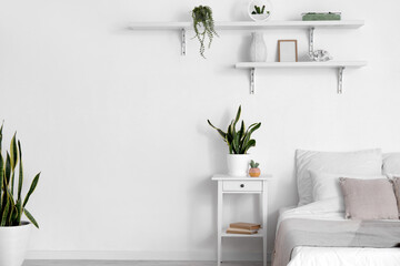 Comfortable bed, nightstand and houseplants near white wall