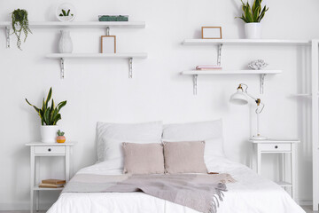 Comfortable bed, nightstands, houseplants and lamp near white wall