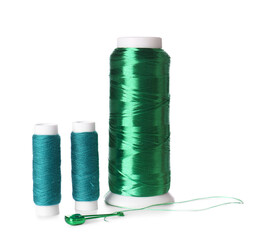 Green thread spools and safety pin on white background