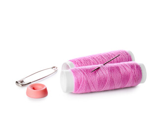 Pink thread spools with needle, button and safety pin on white background