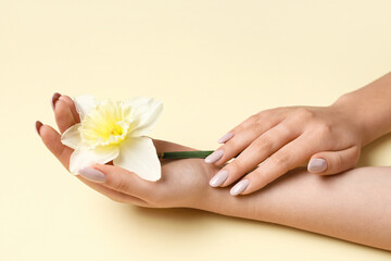 Woman with beautiful manicure and daffodil flower on yellow background