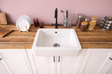 Counters with sink, kitchen utensils and food near pink wall