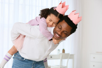 Happy African-American man and his little daughter in paper crowns playing at home