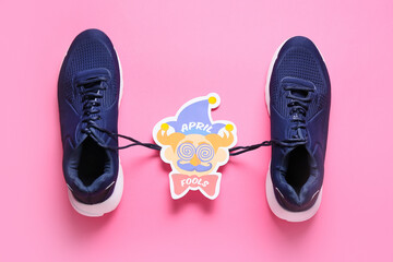 Shoes with tied laces and card with text APRIL FOOL'S on pink background