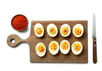 Chopping board with tasty stuffed eggs, paprika and knife on white background. Easter celebration