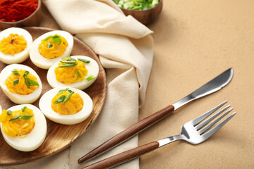 Plate with stuffed eggs, napkin and cutlery on beige background, closeup. Easter celebration