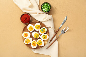 Plate with stuffed eggs, paprika, green onion, cutlery and napkin on beige background. Easter celebration