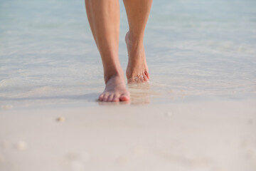 Closeup image of woman with barefoot while walking on the white beach and the sea