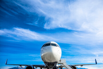 Close up view of the front on an airplane sitting at the airport with clouds and sky in the...